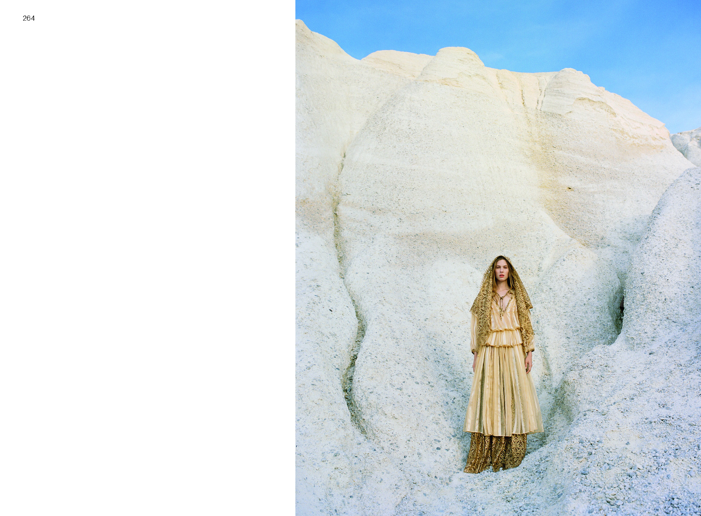 A page from a book with two thirds showing a woman in a long dress and headscarf standing on a barren wall.