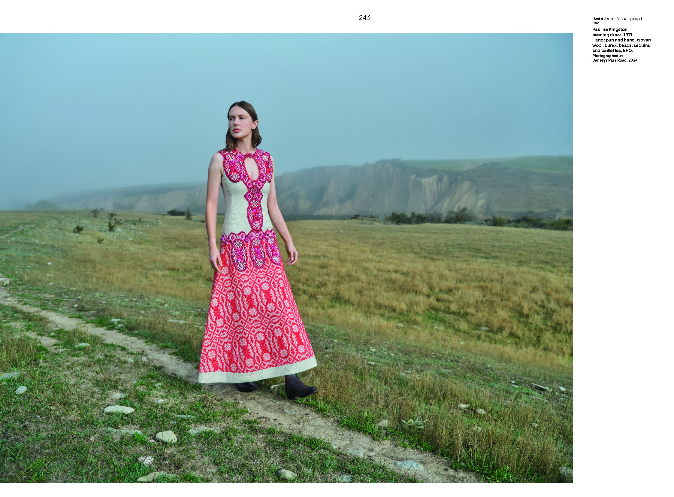 A woman is walking in a field. She is wearing a highly designed long sleeveless dress.
