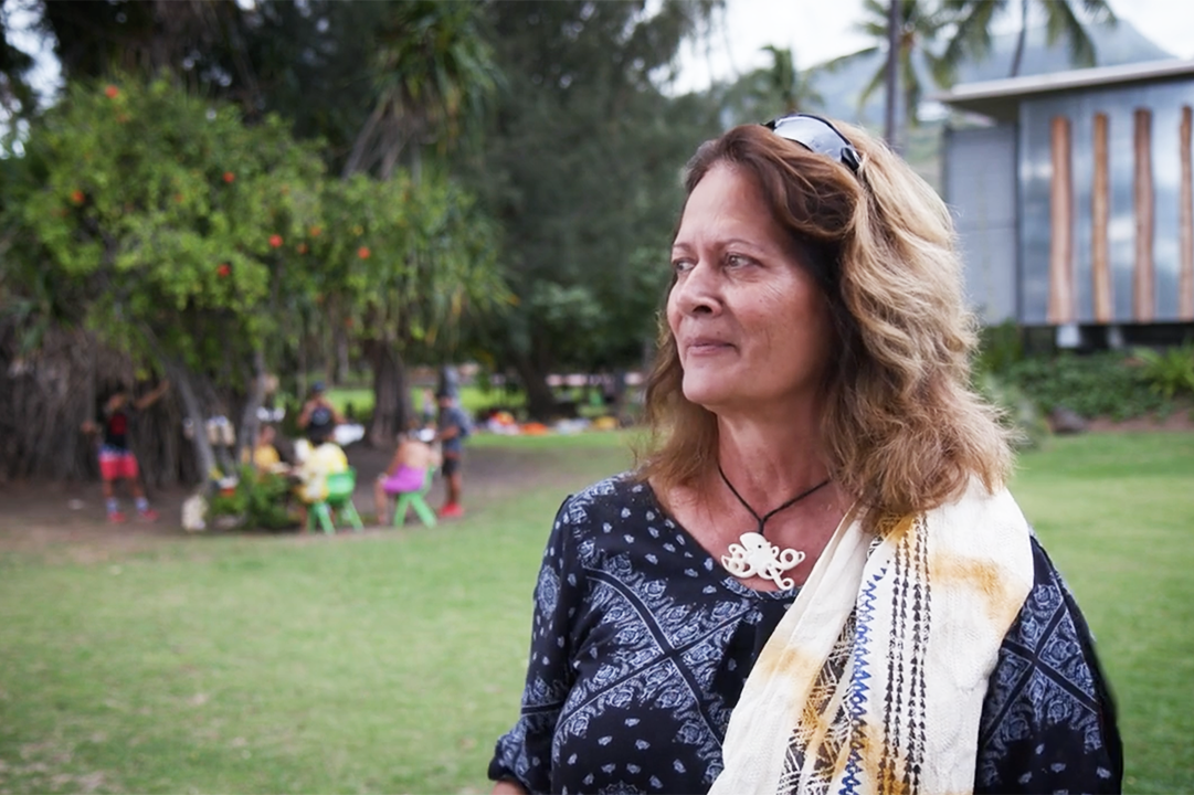 A woman with long hair is standing outside and looking off into the distance.