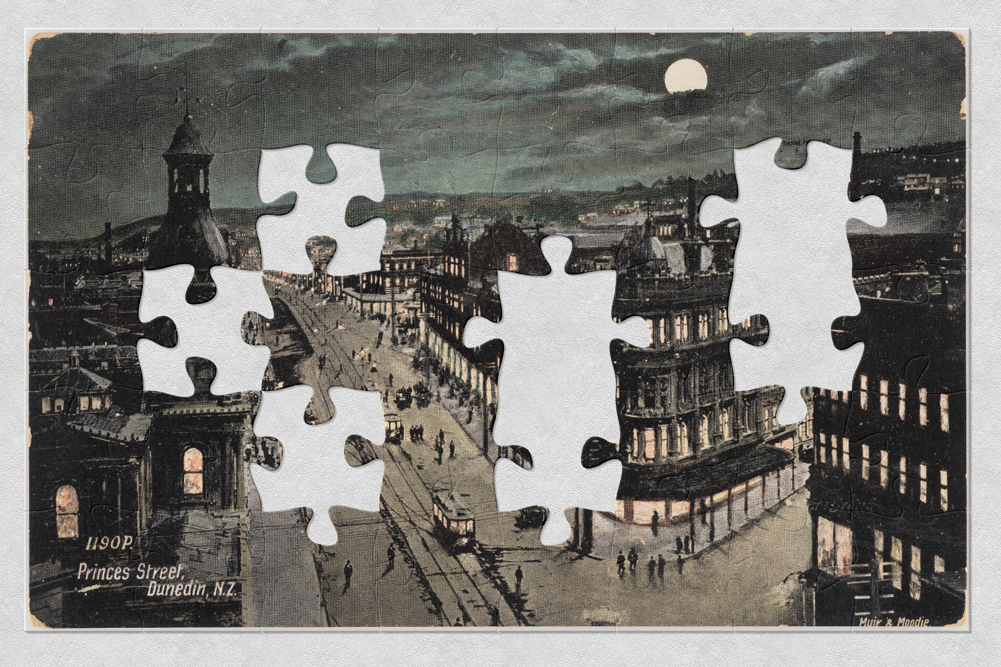 A hand-tinted postcard of a city street at night with the full moon in the sky. There are jigsaw-shaped pieces missing from picture