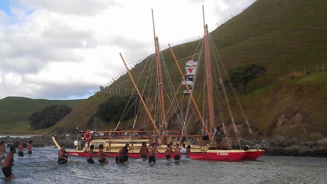 Men are standing in hip-high water and pulling a boat up a river.