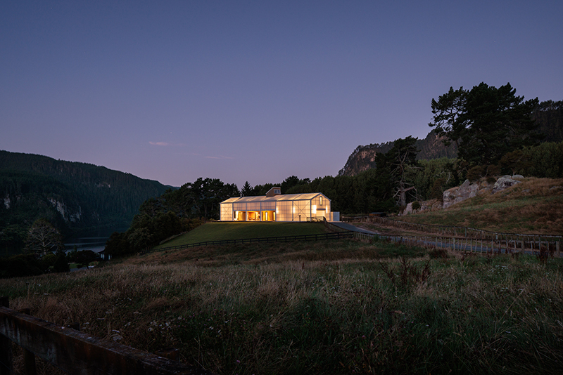 A photo taken at dusk showing a lit-up building on a hill on a farm.