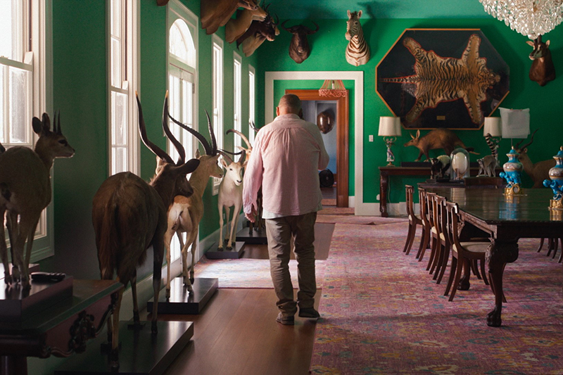 A man is walking away from the camera in a large room with a lot of taxidermied animals and animal skins