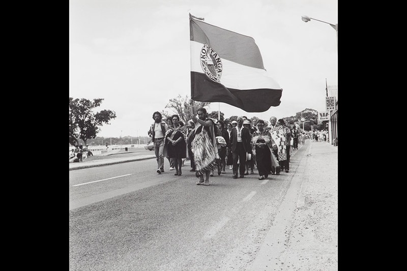 Black and white photo of a group of people on a protest march. They are carrying a large flag.