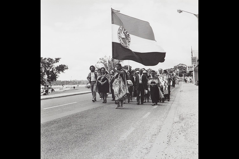 Black and white photo of a group of people on a protest march. They are carrying a large flag.