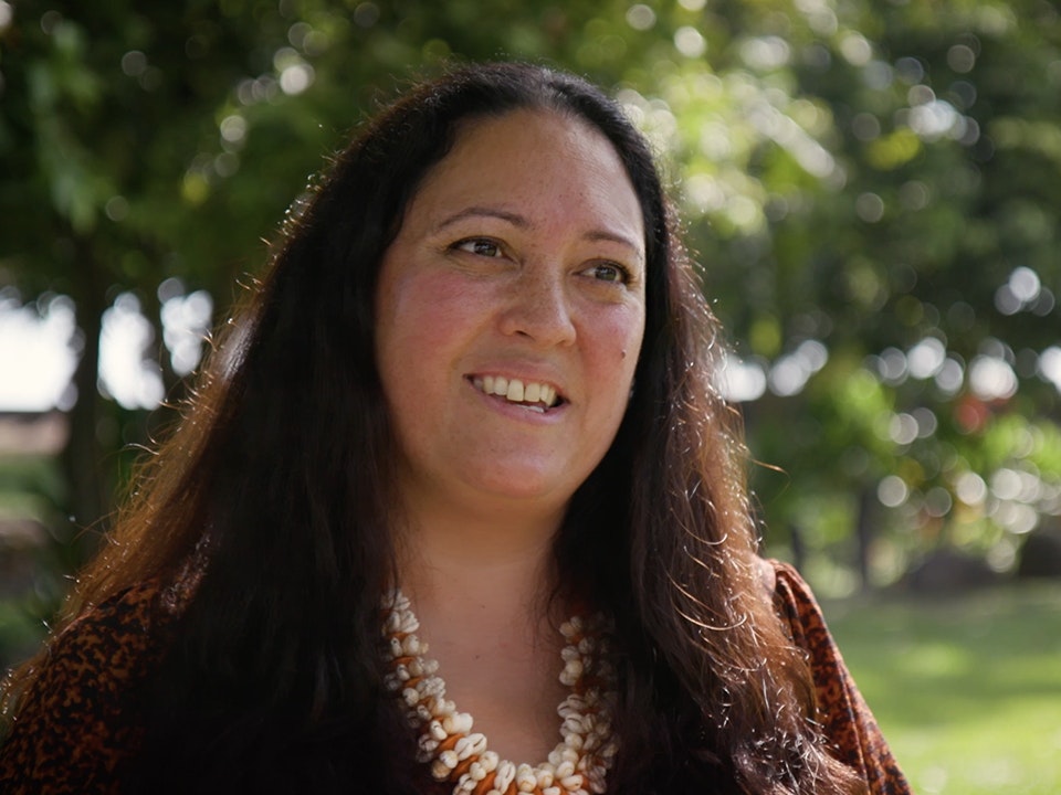 Still from video with Tui Emma Gillies Head and shoulders of a woman with long, dark hair wearing.a shell necklace.
