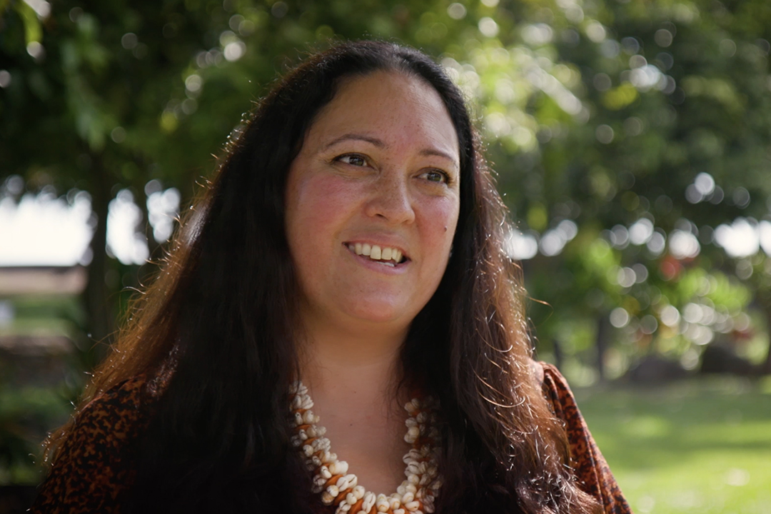 Head and shoulders of a woman with long, dark hair wearing.a shell necklace.