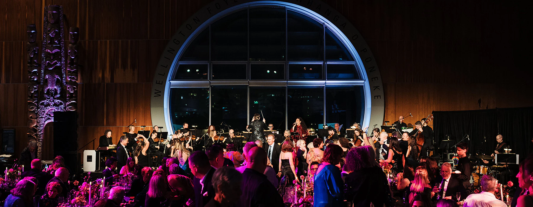 A large group of people at a party in a large foyer with a round window at the back.