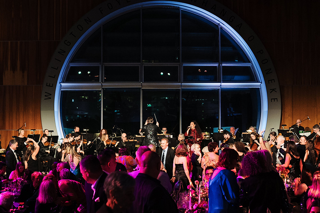 A large group of people at a party in a large foyer with a round window at the back.