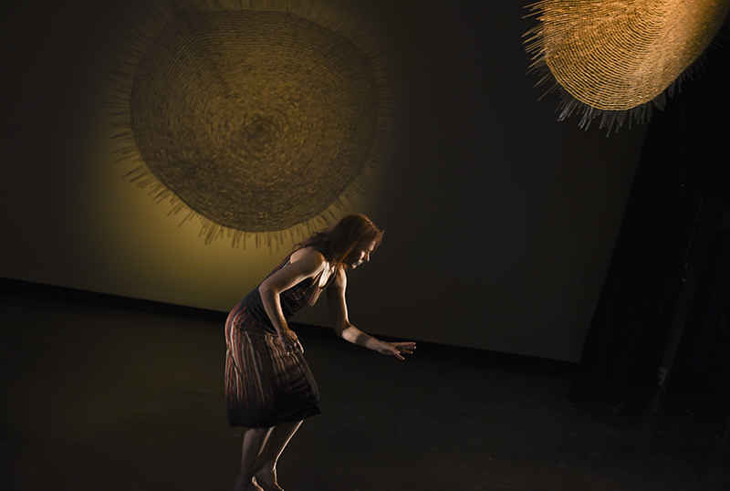 A person is dancing on stage with large woven circles behind them.