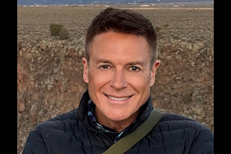 Head and shoulders photo of a man in a dark top smiling at the camera.