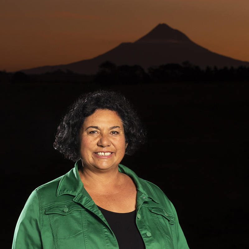 Head and shoulders of a woman in bright green cardigan standing in front of a silhouette of a mountain.