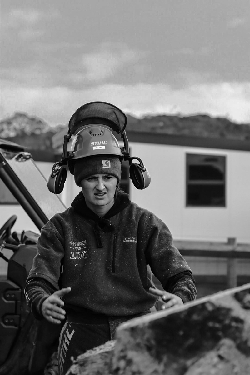 A black and white photo of a person in a hardhat with headphones to the side working on a farm.
