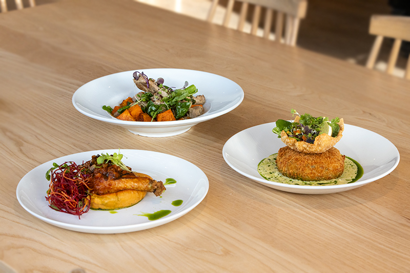 Three dishes of artfully arranged food on white plates sitting on a table.