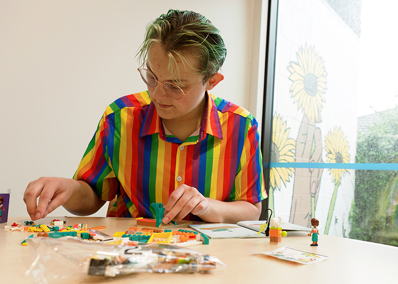 Child in rainbow-coloured shirt playing with lego. 