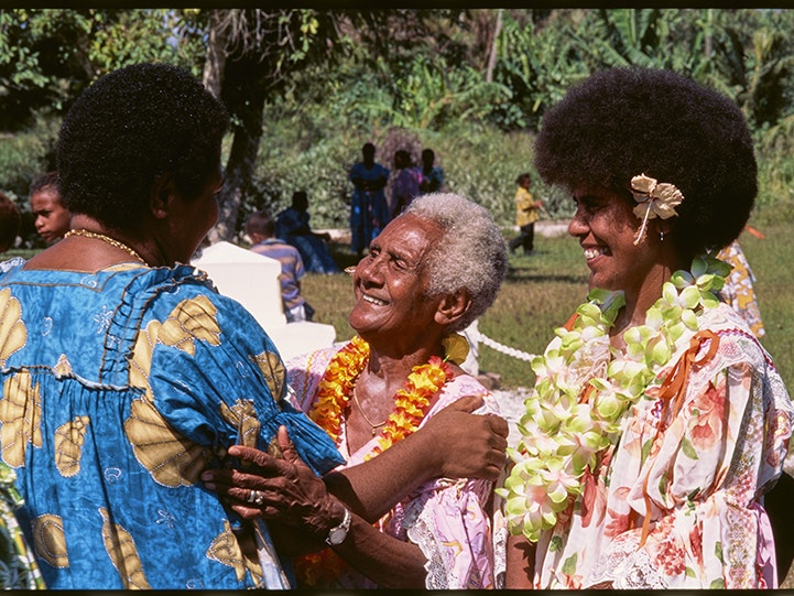 Three women dressed for an occasion, Vanuatu, Glenn Jowitt, Vanuatu 1997. Gift of Glenn Jowitt Estate, 2015. Te Papa (E.007649) Three women in brightly coloured dresses are greeting each other on a Pacific Island.