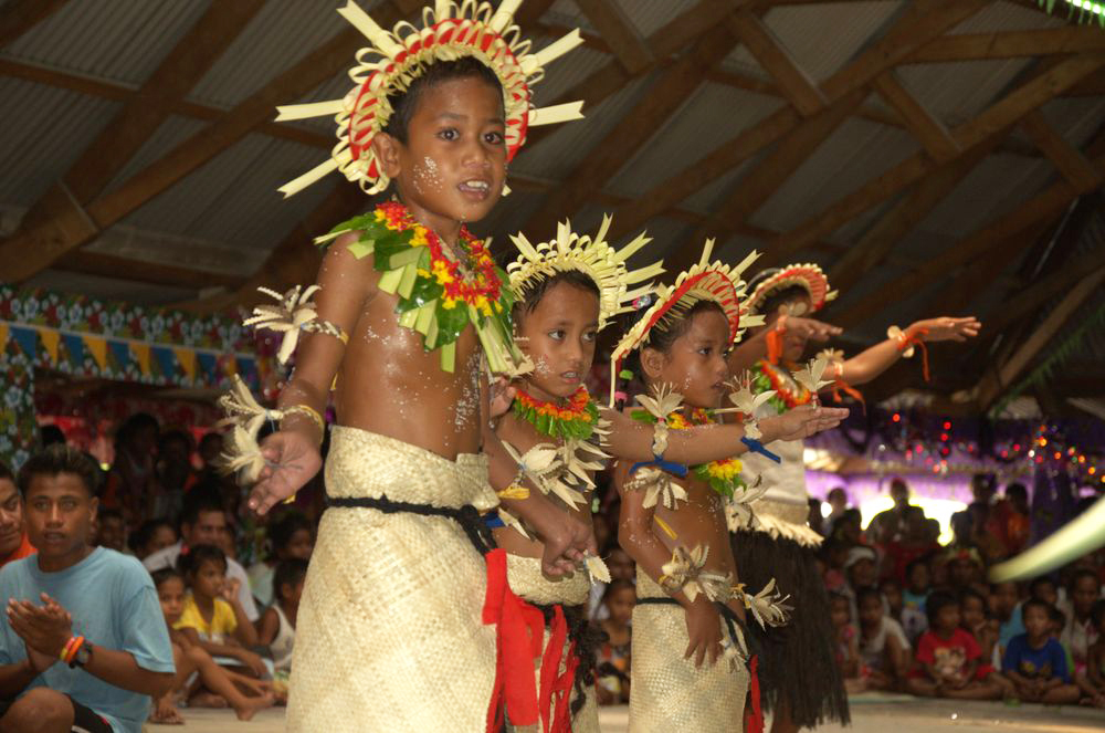 Children in traditional Kiribati costume are performing for people.