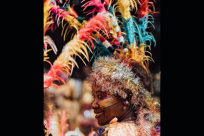 Vanuatu woman with her face painted with tribal motifs looking at the camera wearing a colourful head piece with colourful feathers and sparkly tinsel.  