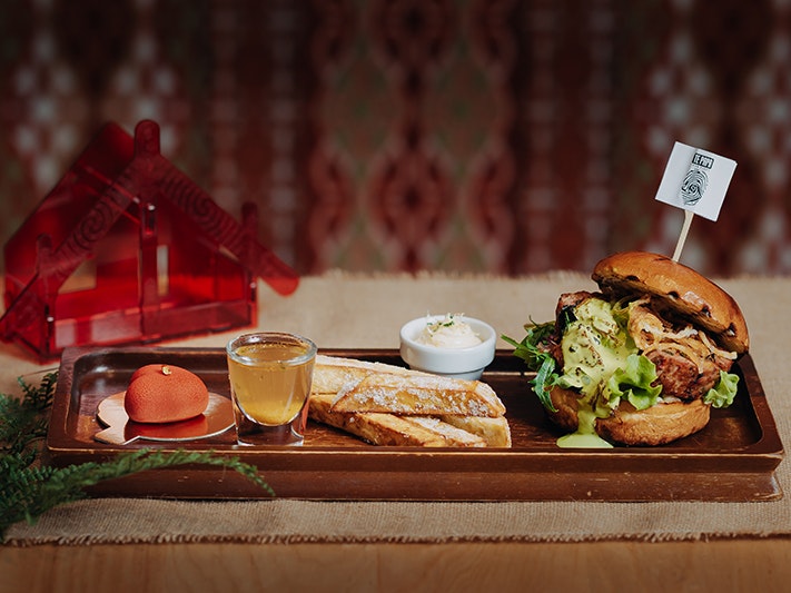 Āhuru Kai Kōhua Poaka – Te Papa Café’s 2025 Burger Wellington entry. Photo by Victoria Saunders A meal including a burger, some bread, and a heart-shaped desert on a platter on a table.