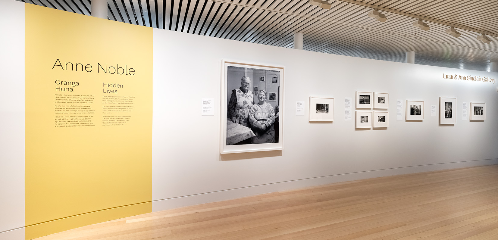 A photographic installation in a gallery with a large yellow sign and several framed black and white photos arranged on the wall.