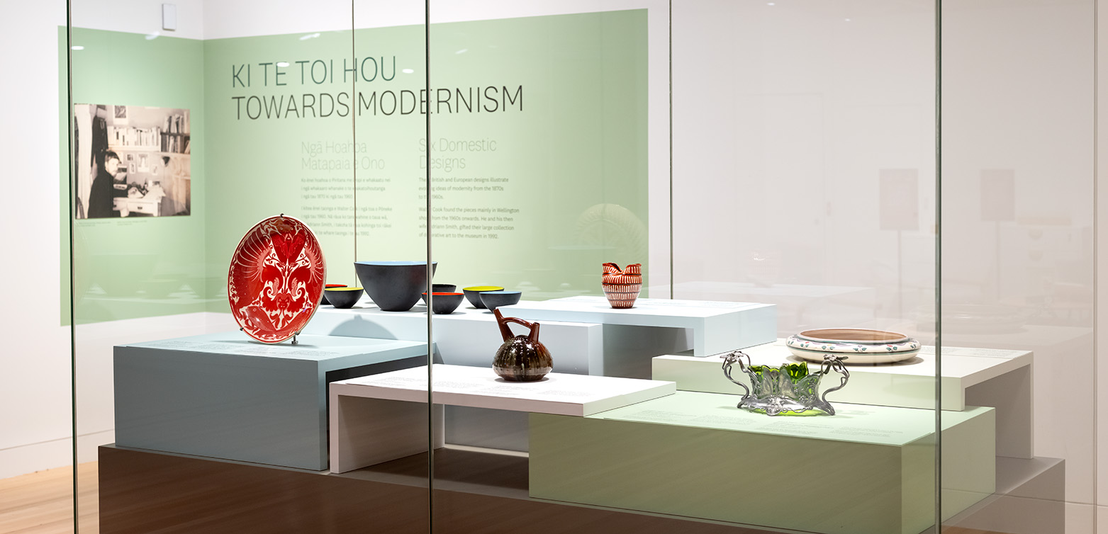 A glass cabinet in a gallery with several pieces of crockery or porcelain or silver ware on blocks of differing heights.