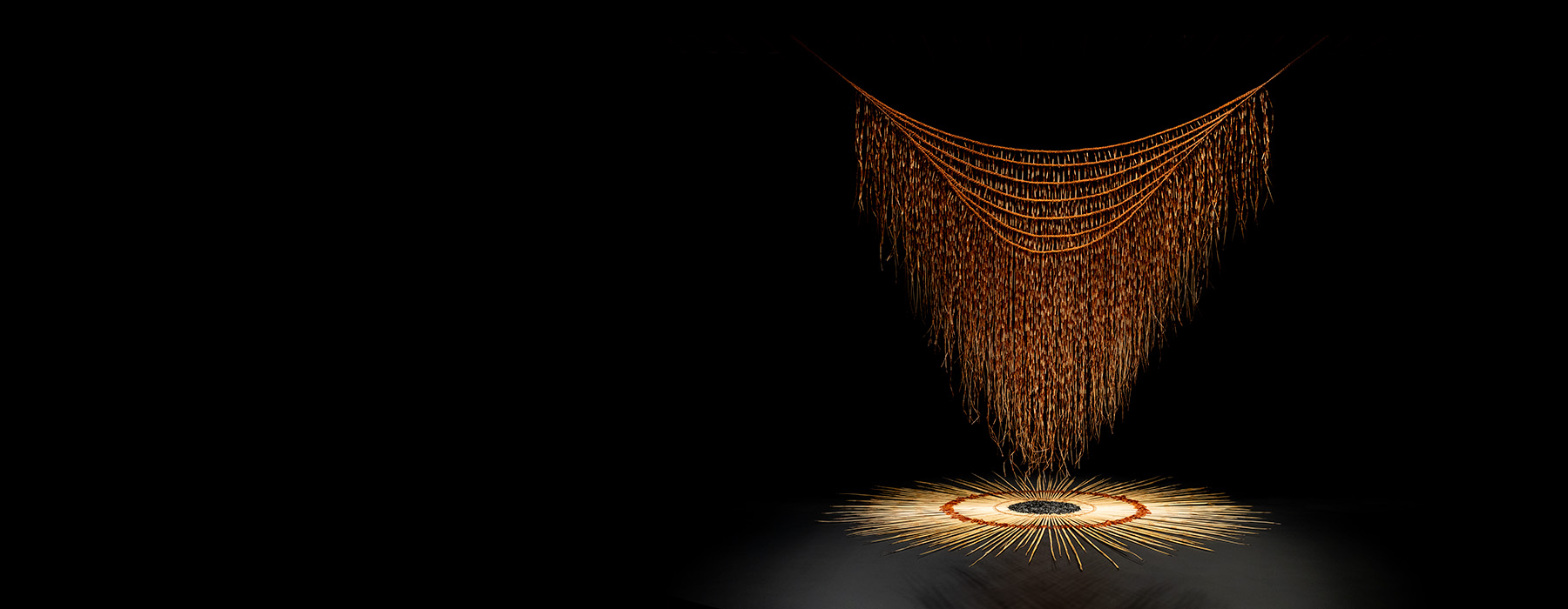 A black rectangle with an artwork of a woven cloak hanging over a circle of similar woven material.