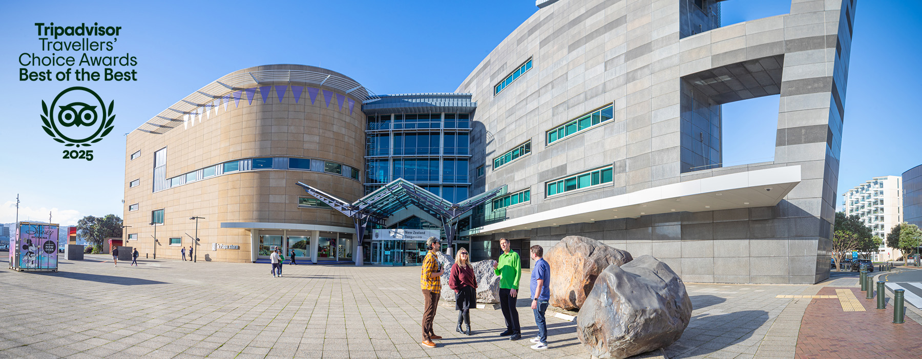Four people are standing by the giant rocks outside the Te Papa muesum on a sunny day.