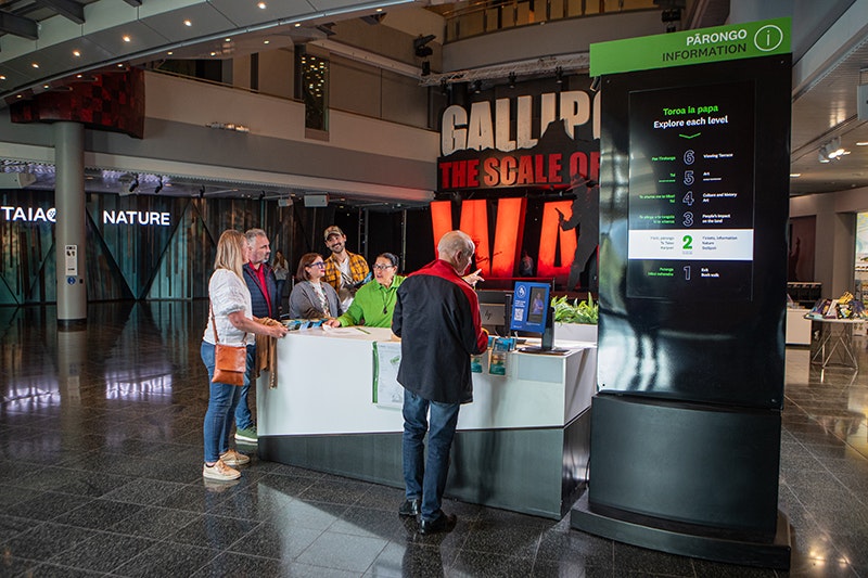 Several people are standing by a desk in a museum where a staff member is telling them information.
