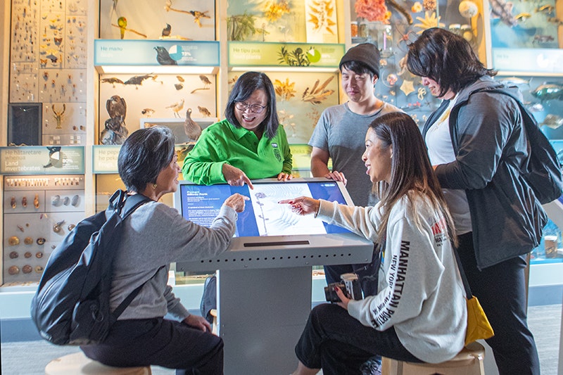 Several people are gathered around a screen that is describing what they can see on the wall behind them.