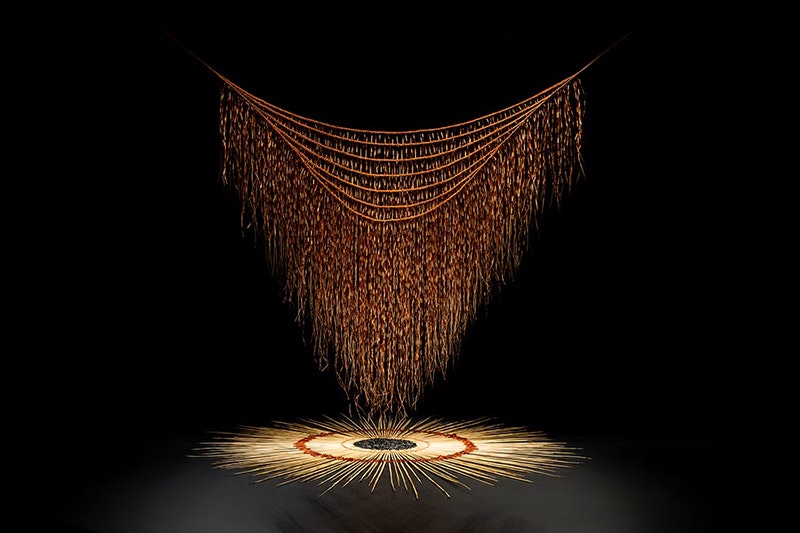 A black rectangle with an artwork of a woven cloak hanging over a circle of similar woven material.
