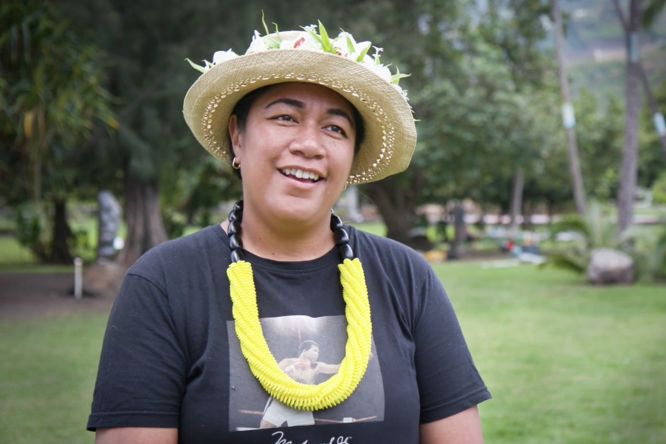 A woman in a tshirt and straw hat is talking to a person off camera.