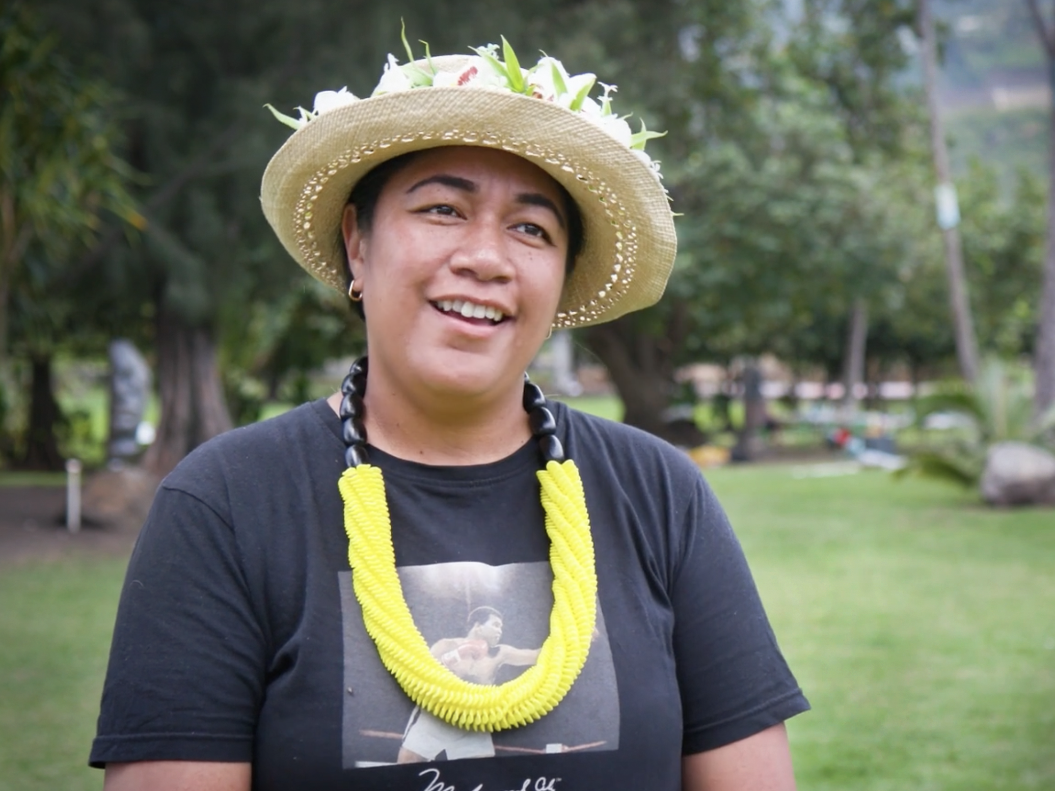 Still from the interview with Cora-Allan. Te Papa A woman in a tshirt and straw hat is talking to a person off camera.