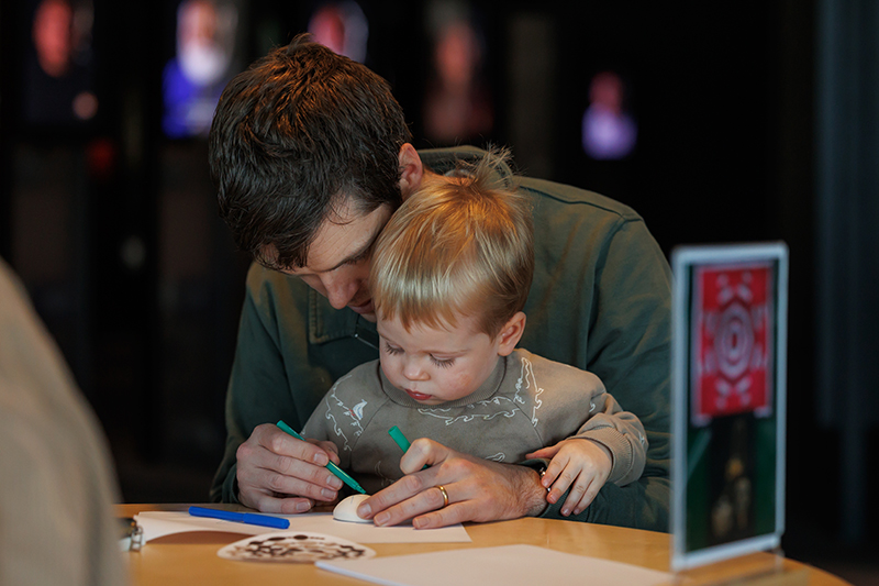 An adult has a child on their knee and is helping the child colour in a piece of clay.