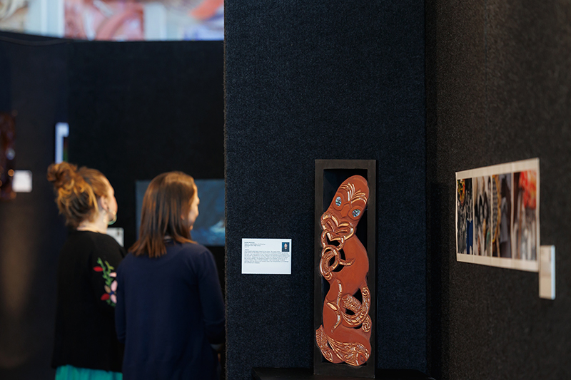 Two people are looking at artwork hung on a black wall.