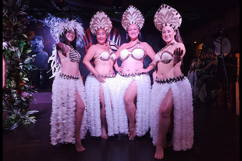 Four women in traditional dance costume are posing together and smiling at the camera.