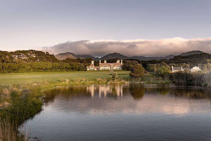 A large house is set back from a lake on a large property.