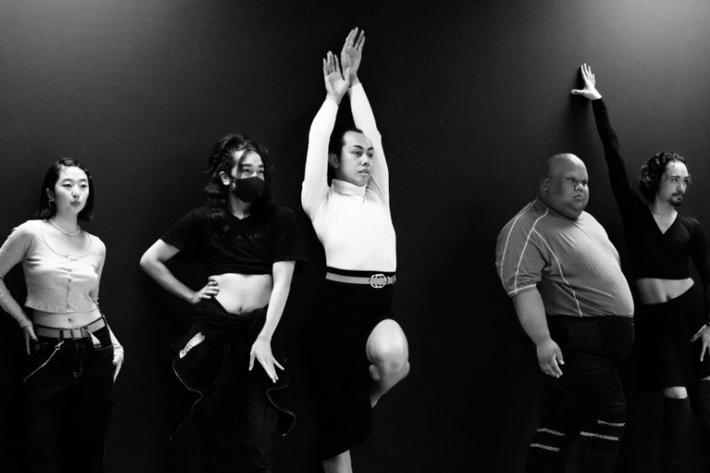Black and white photo of five people in a vogue workshop in various poses.