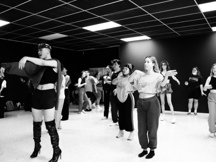 House of Marama Wellington Ballroom Workshops, 2022. Photo by K-Ci Marama A black and white photograph of people in a dance studio. The lead person is wearing knee high boots and a black hat and is demonstrating a move.