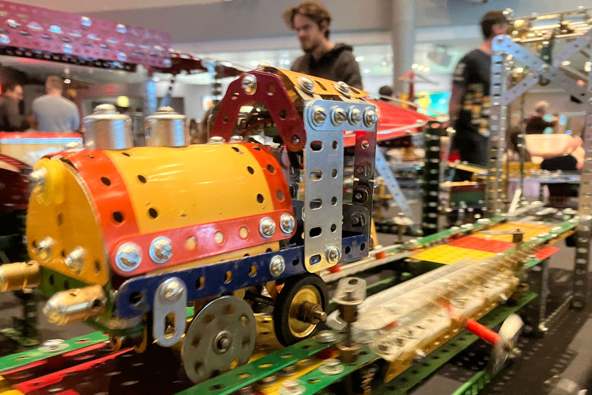 A yellow, orange and blue meccano train zooming along meccano tracks towards the viewer.