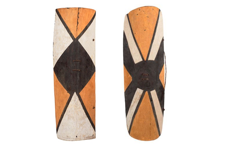 Two wooden shields with orange, black, and white geometric shapes painted on them.