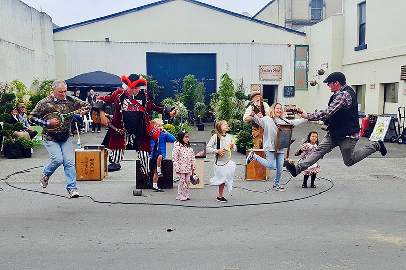Several people are playing instruments and jumping in the air with a lot of kids doing the same thing.