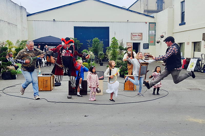 Several people are playing instruments and jumping in the air with a lot of kids doing the same thing.