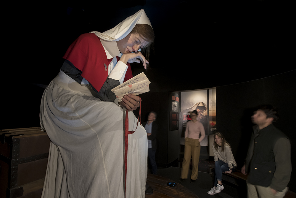 Exhibition visitors are standing around a giant model of a World War One nurse reading a letter.