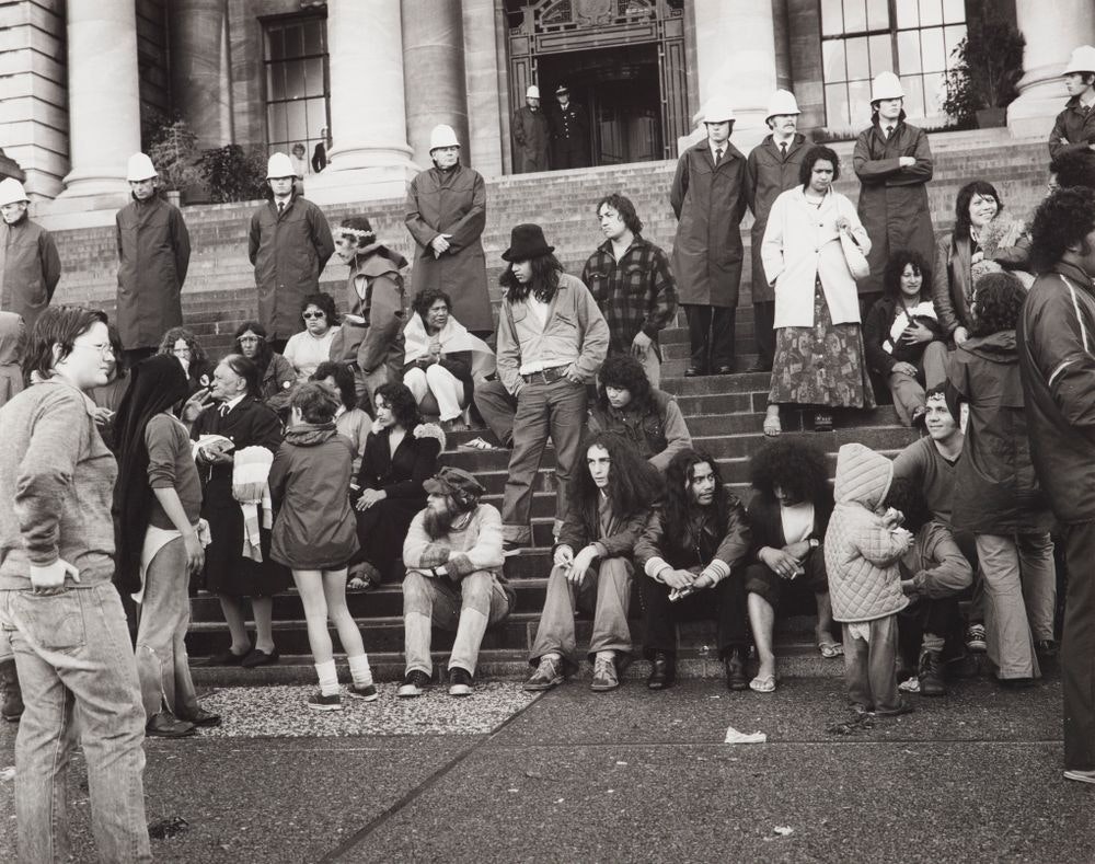 Black and white photo of people standing and sitting on the steps of parliament.