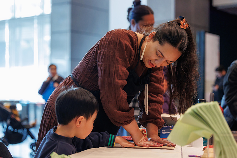 A woman is helping a young child make a print at a large table.