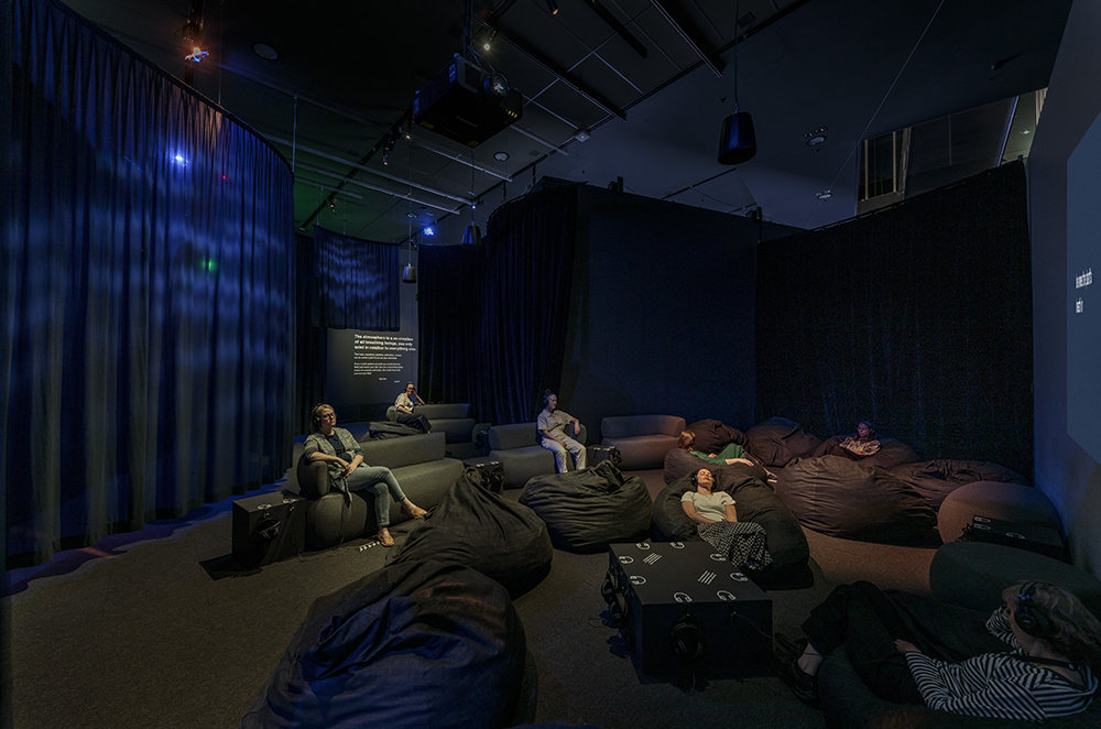 Several people are sitting on sofas and beanbags and listening and looking up.