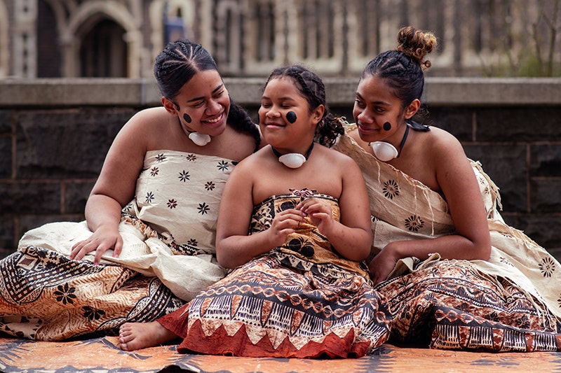 Three women in Fijian clothing are sitting close together and smiling at each other