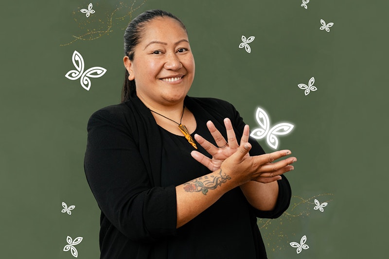 A woman is using her hands to say sign language and smiling at the camera.