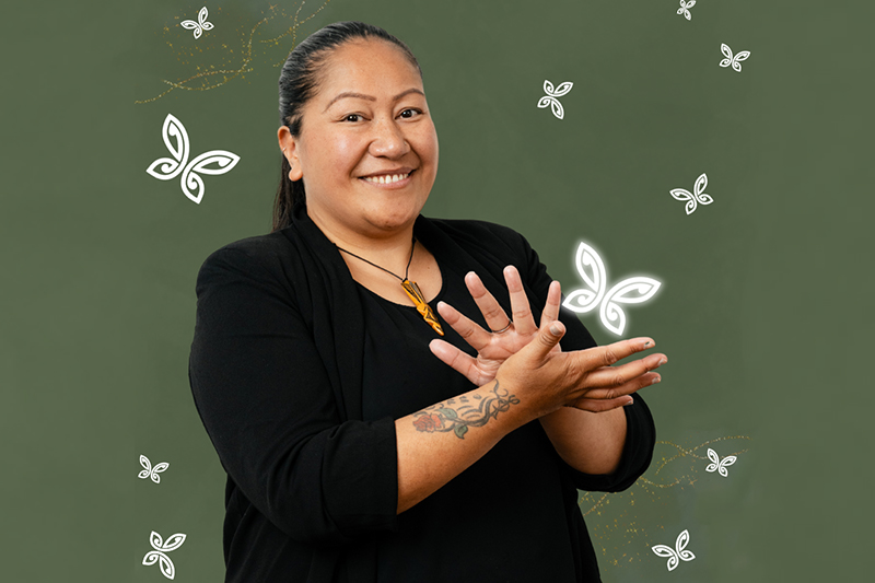 A woman is using her hands to say sign language and smiling at the camera.