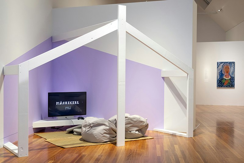 A whare-like structure with a TV screen inside it, and two bean bags and cushions on the floor